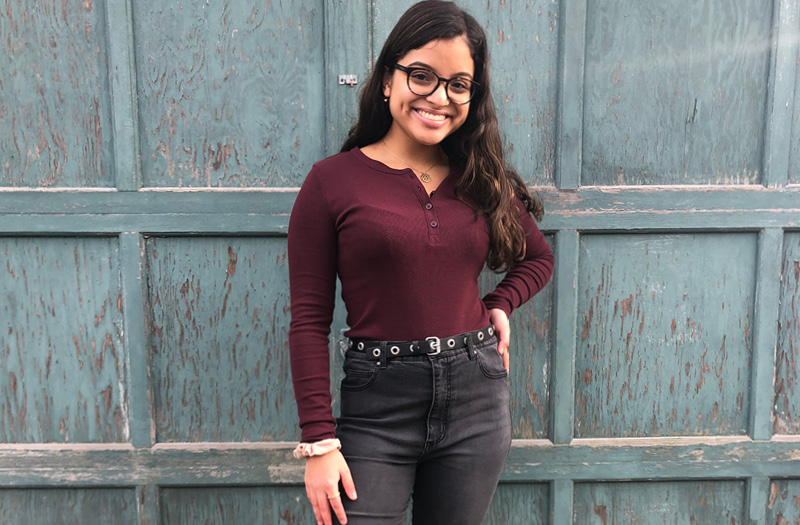 A young woman wearing glasses posing in front of a garage.